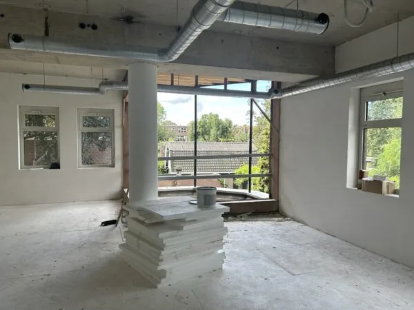 Binnenruimte in verbouwing aan de Bergse Dorpsstraat met zicht op daken en groen buiten.